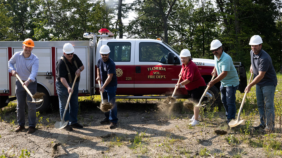 group of six people wearing hard hats and shoveling dirt in front of a Florida Volunteer Fire Department truck